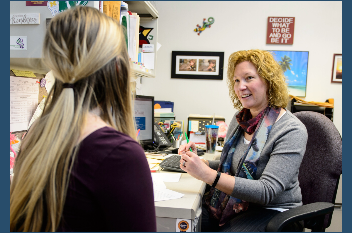 Woman with red curly hair talking to fair-haired student with back to camera